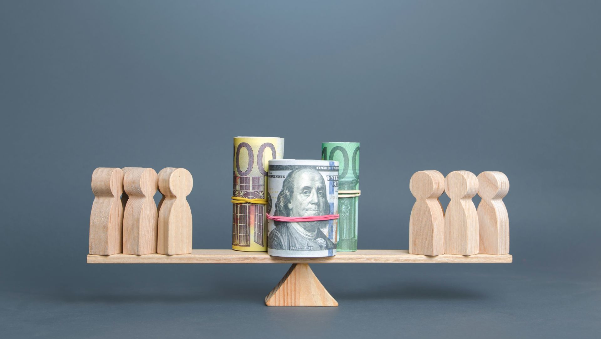 Wooden figures and rolled currency balanced on a scale, symbolizing fair distribution of assets in special needs trusts.