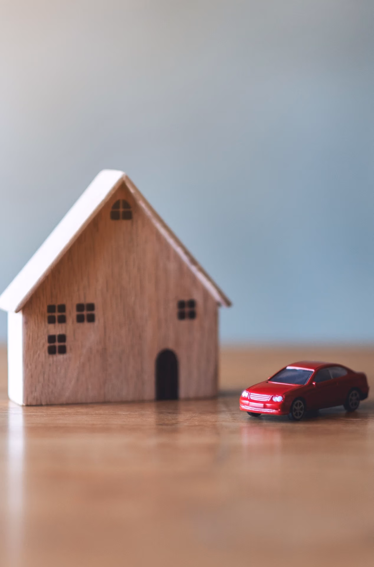 Wooden house model and red toy car symbolizing estate and assets