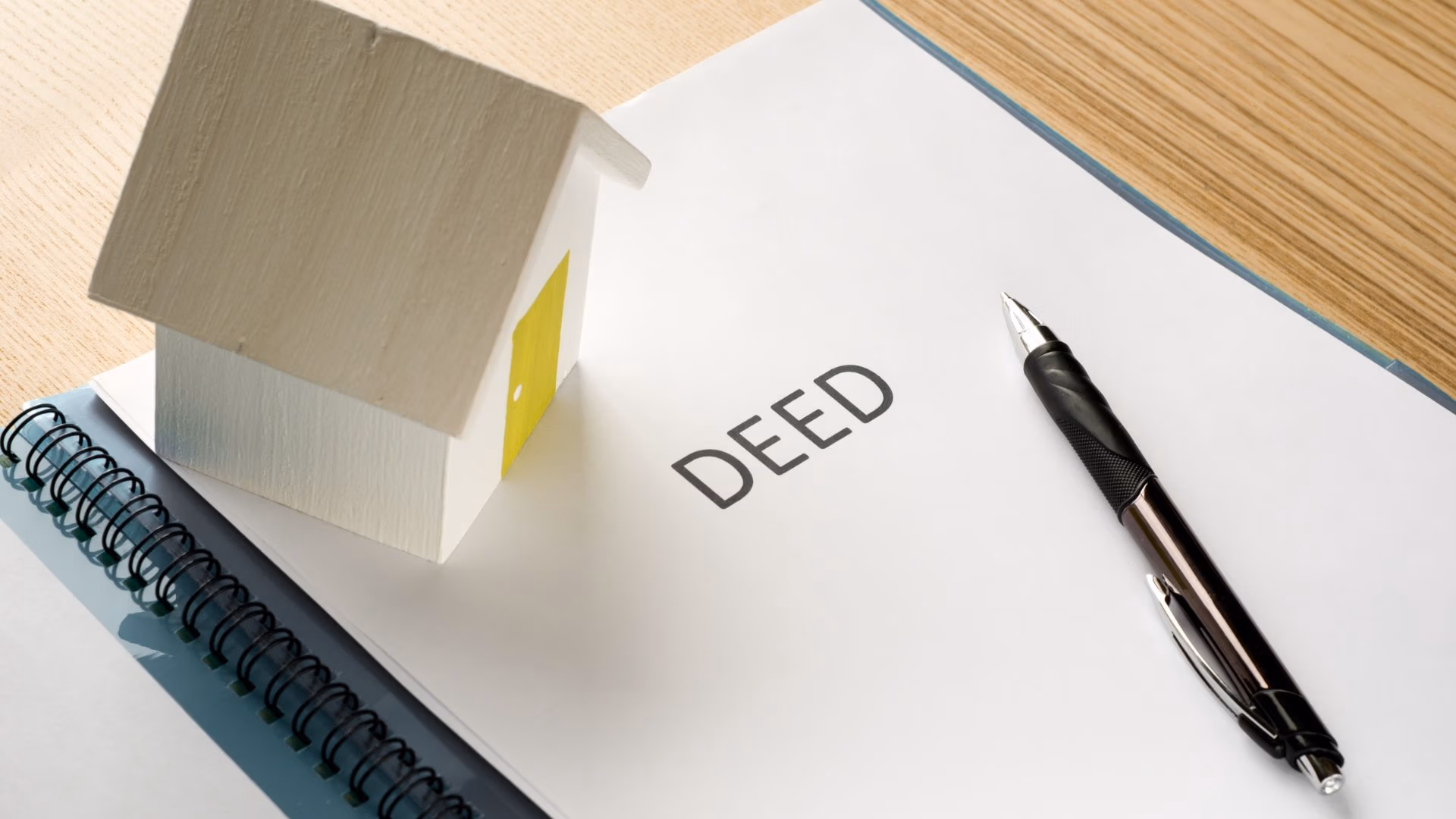 Mini house model and pen placed on a document labeled “DEED,” symbolizing property ownership and estate planning.