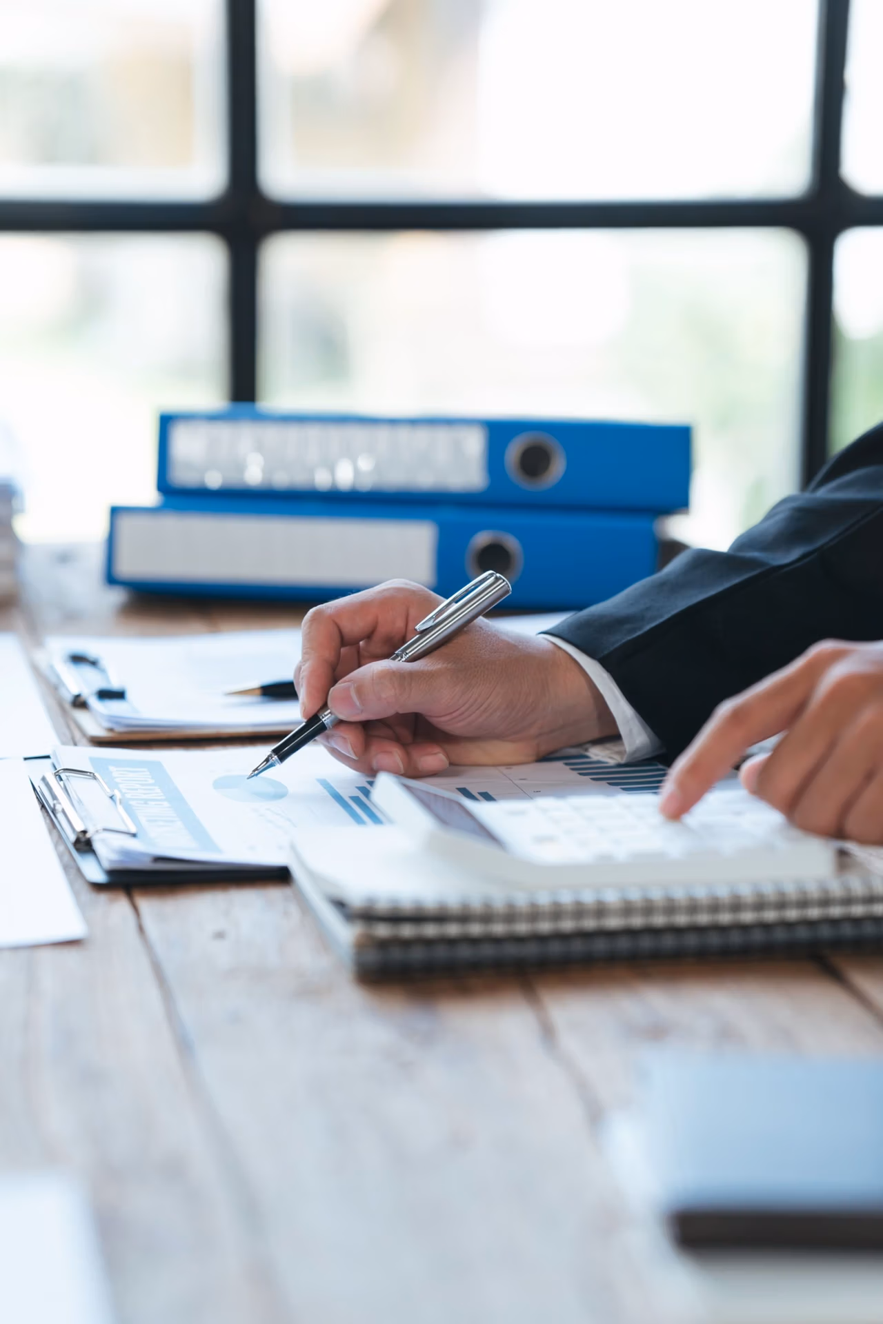 Person reviewing financial documents and using a calculator with files organized on the desk.