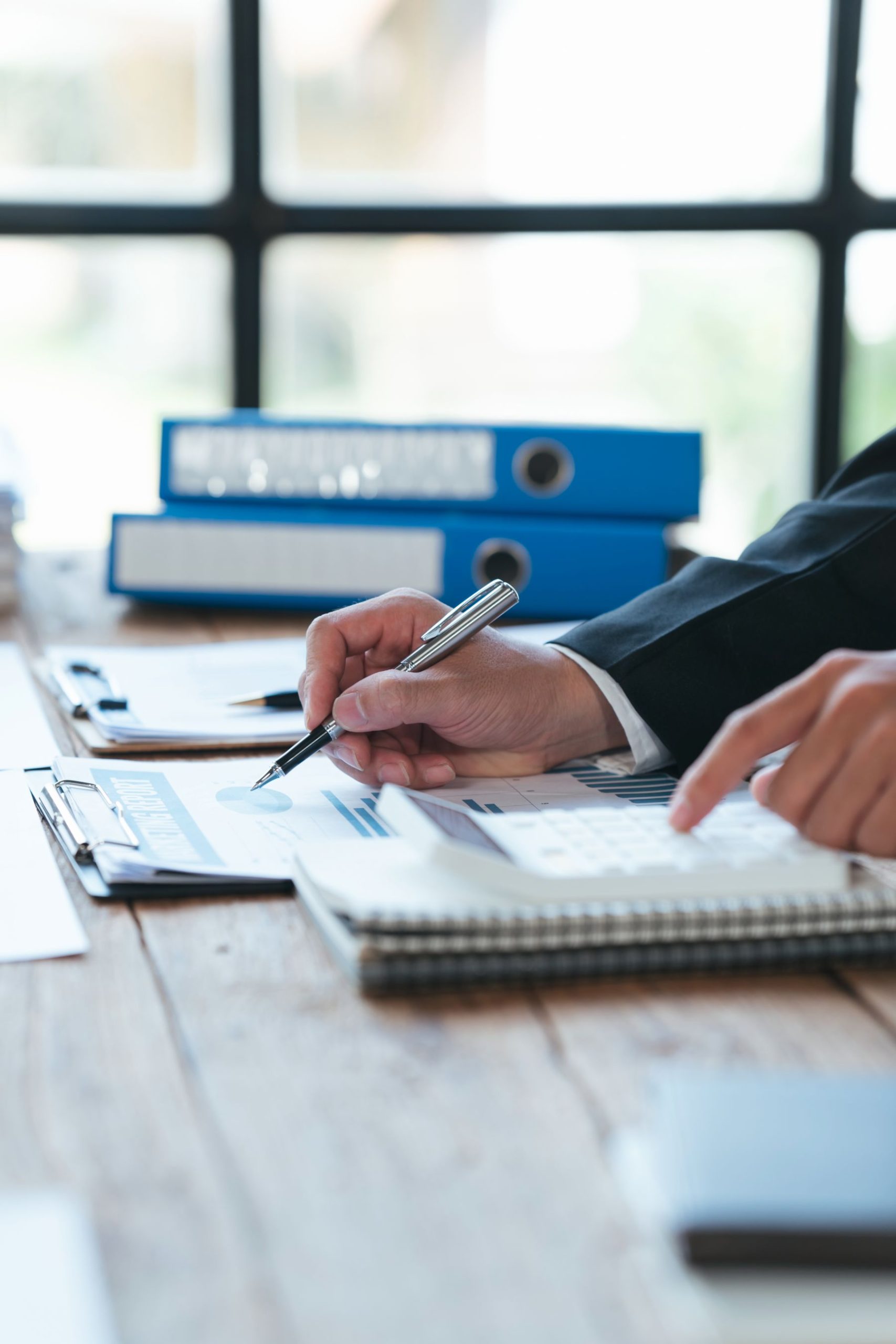 Person reviewing financial documents and using a calculator with files organized on the desk.