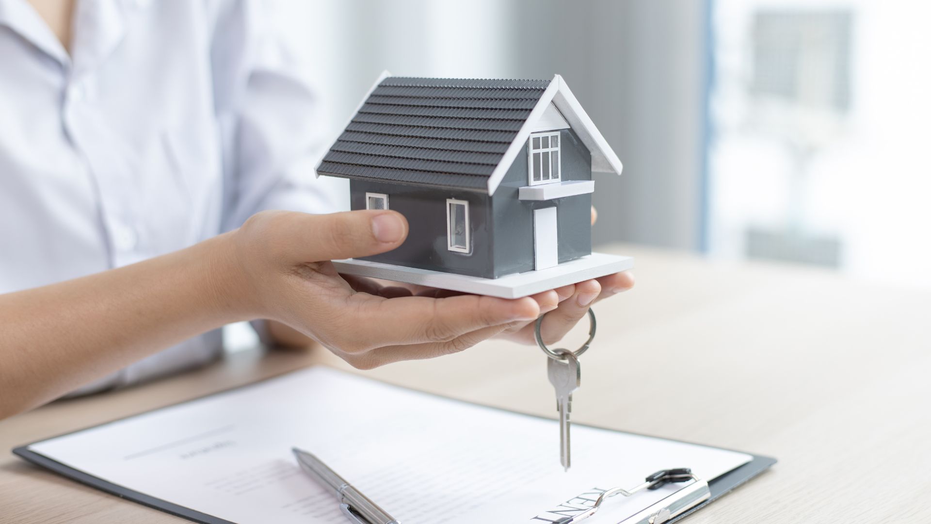 Hands holding a miniature house model with a key, symbolizing home ownership and estate planning.