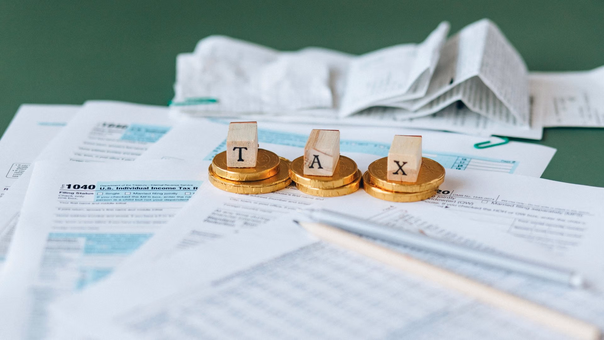 Wooden blocks spelling “TAX” on gold coins placed over tax forms and receipts.