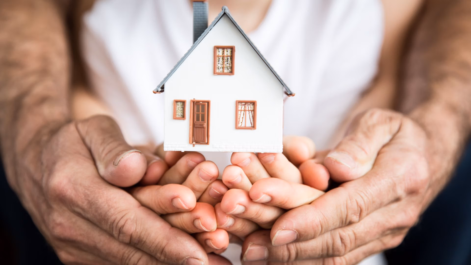 Hands of adults and a child holding a small house model, symbolizing family home protection and legacy.