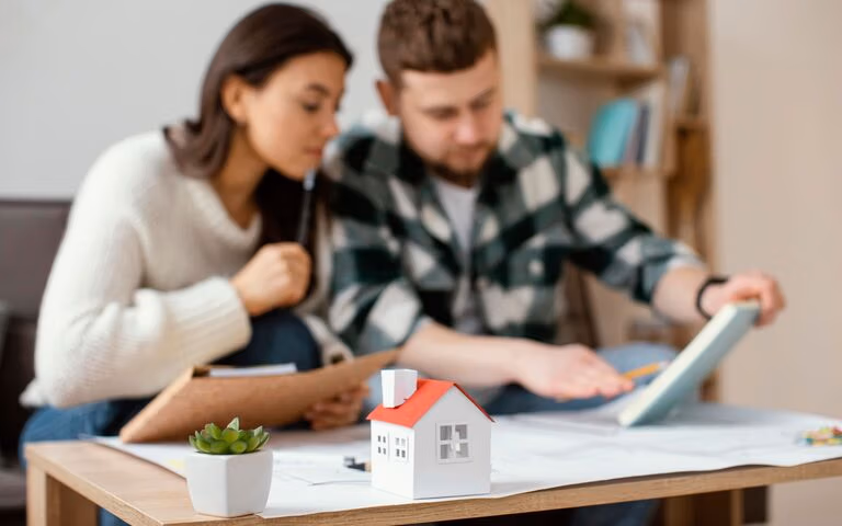 Couple reviewing estate planning documents at home with a small model house on the table.