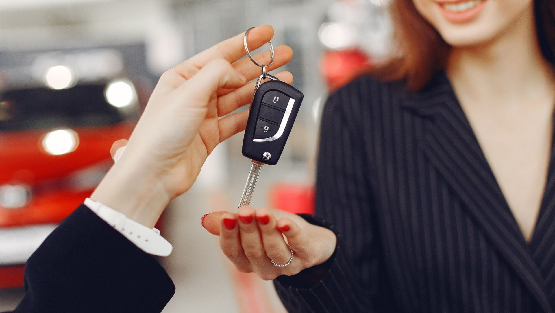 Person handing over car keys to a smiling woman, symbolizing vehicle ownership transfer.