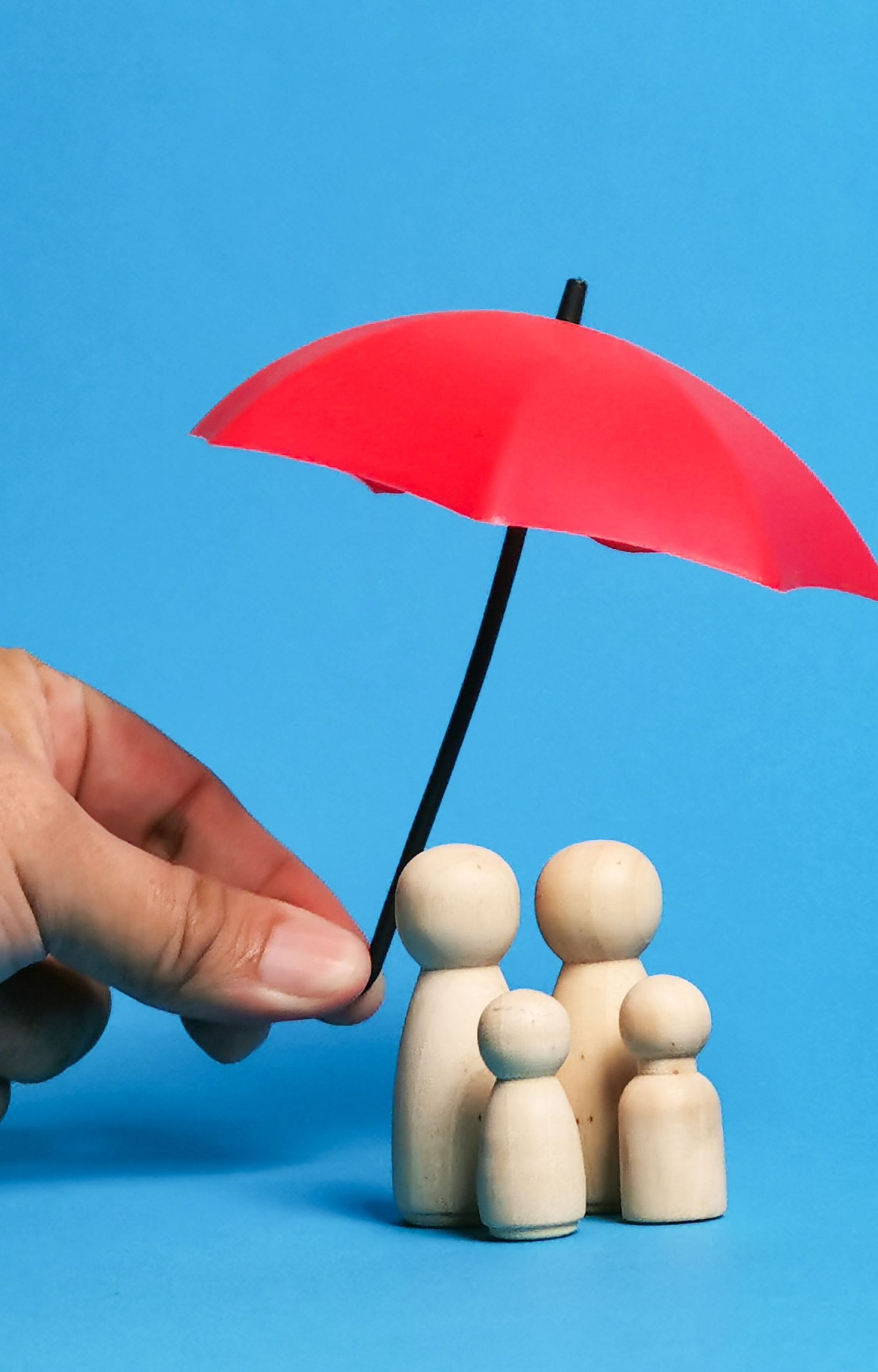Hand holding a red umbrella over wooden family figures, symbolizing protection and estate planning security.