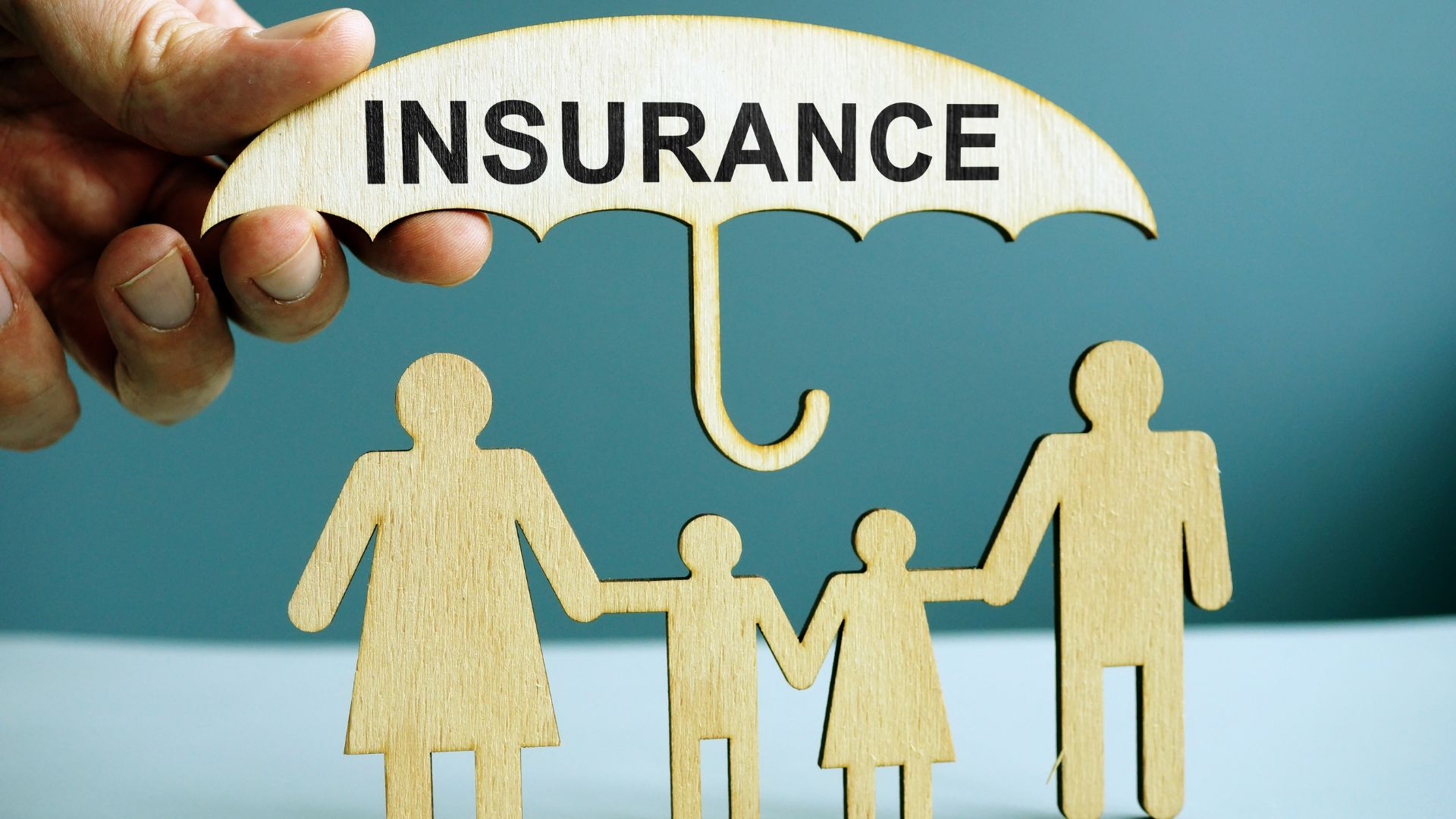 Wooden family figures under an umbrella labeled “Insurance,” symbolizing family life insurance protection.