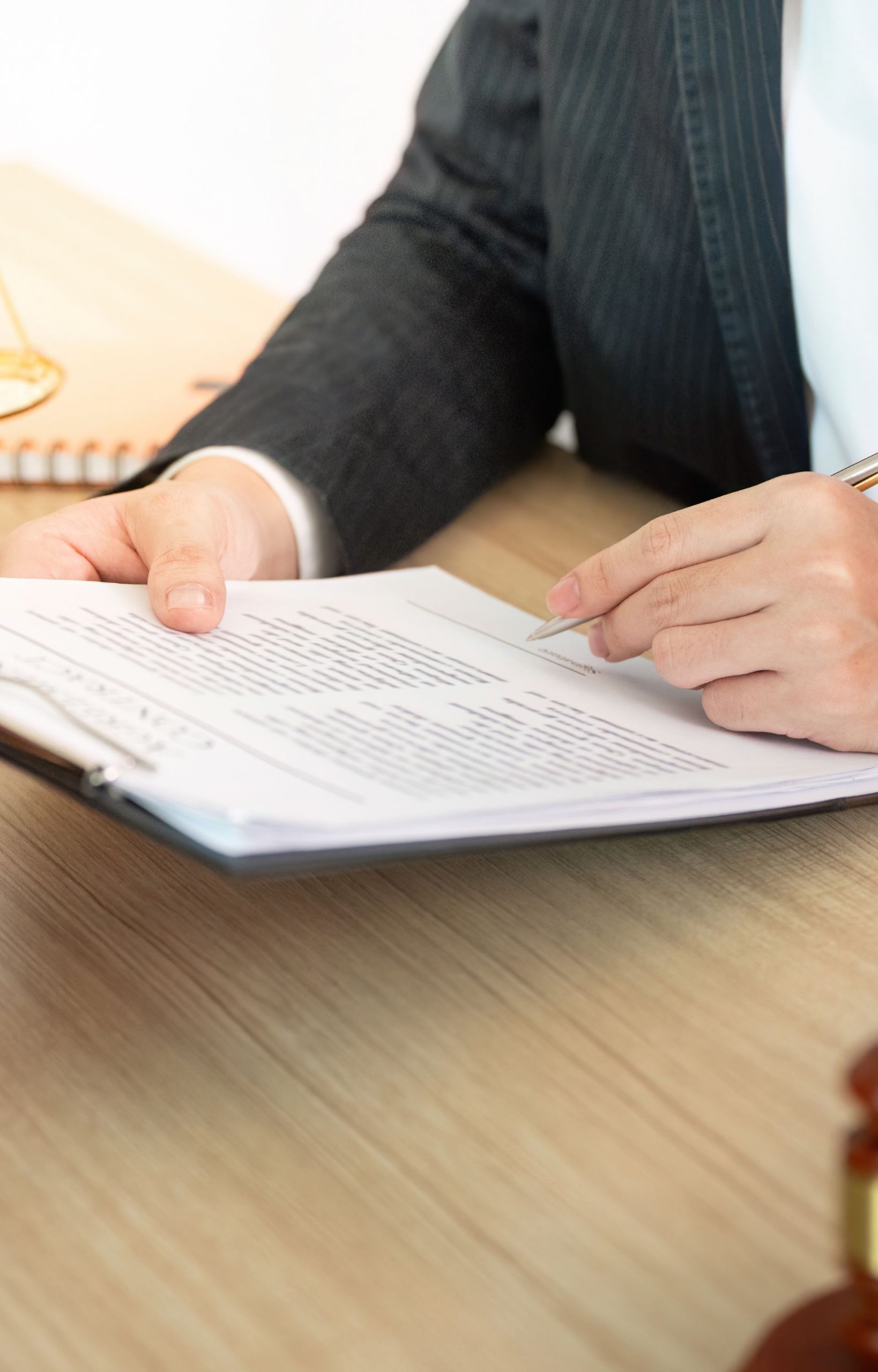 Lawyer reviewing and preparing to sign legal documents on a wooden desk with paperwork in hand.