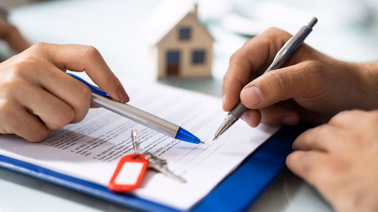 Signing real estate documents with house keys and miniature home model on table, symbolizing property transfer.