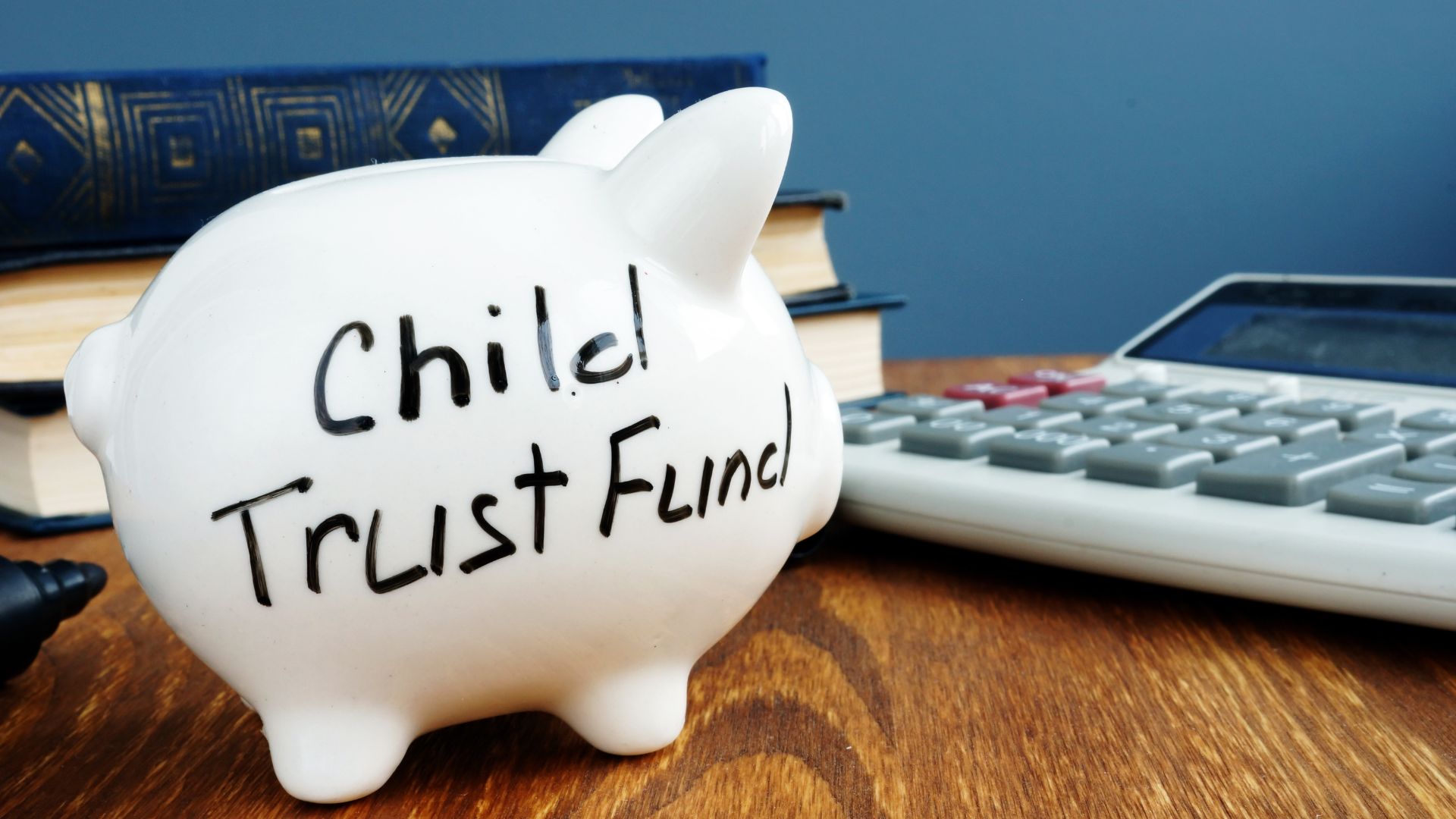 White piggy bank labeled "Child Trust Fund" beside books and a calculator, symbolizing financial planning for children’s future.