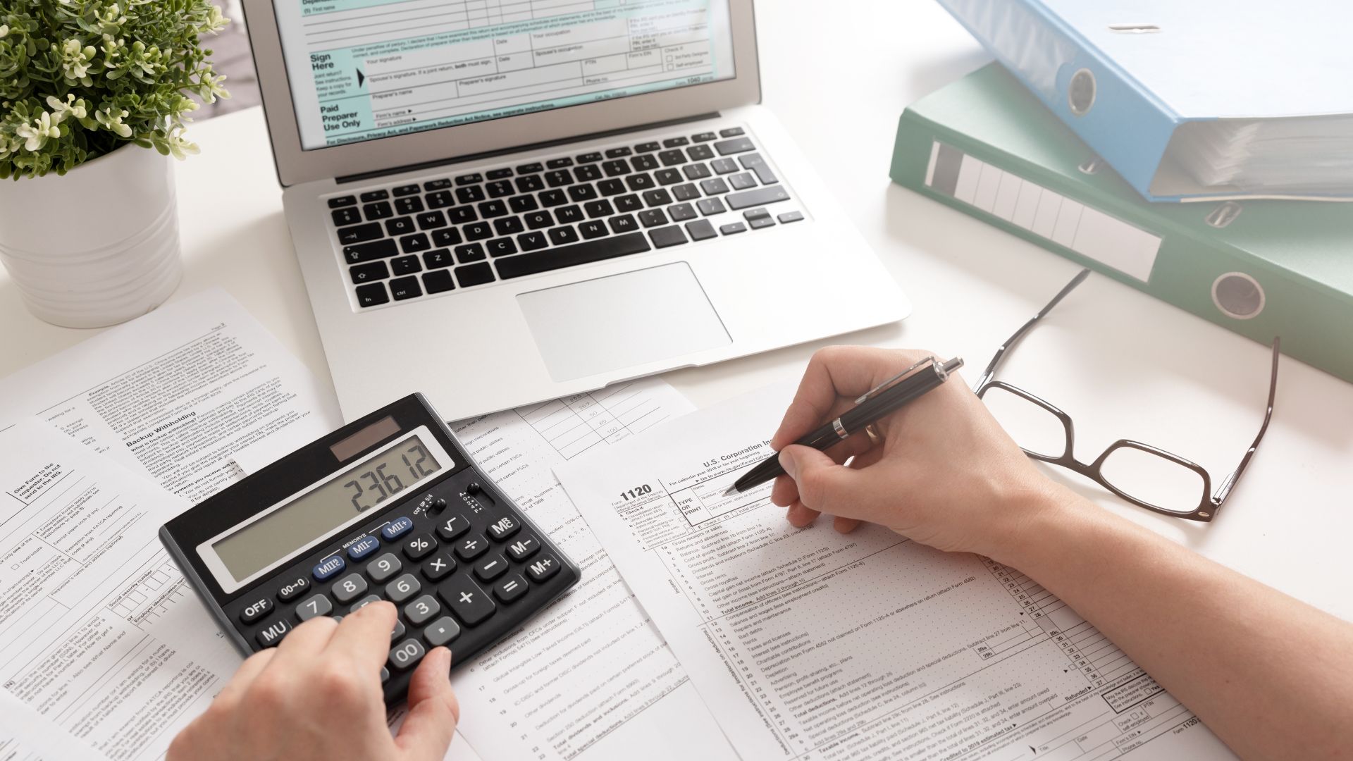 Person calculating probate tax with calculator, laptop, and financial documents.