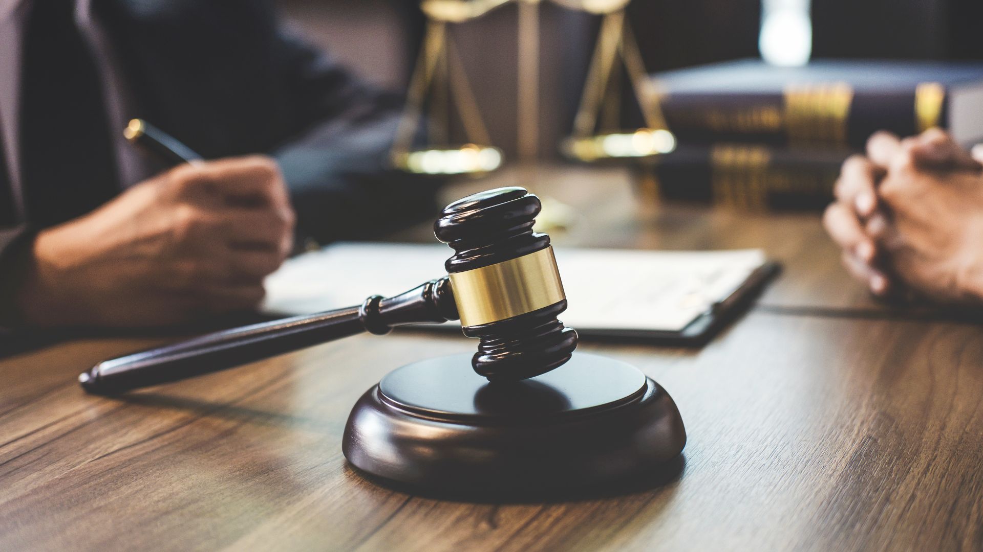 Close-up of a judge’s gavel on a desk with legal documents and people discussing law in the background.