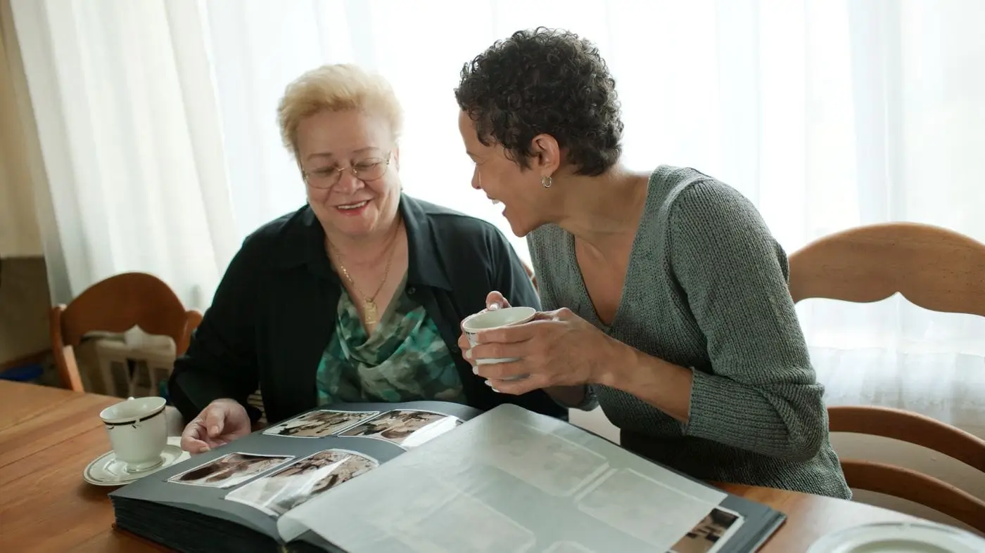 Two women look through a family photo album at a kitchen table